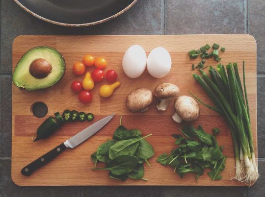 Flat lay of fresh ingredients with avocado, herbs, jalapeno, and egg