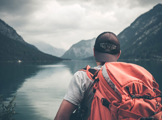 Hiker with a heavy backpack looking out at mountains and still water
